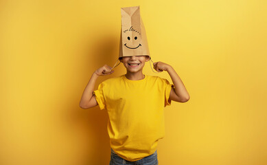 Child hides his head inside a shopping bag. yellow background