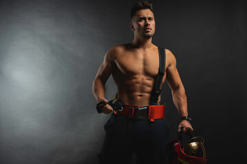 Fototapeta na wymiar portrait of a muscular, handsome firefighter on a dark background, holding a fire helmet, looking to the side