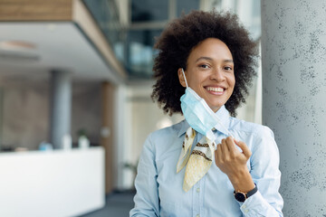 Happy African American businesswoman taking off protective face mask while looking at camera.