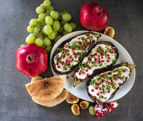 Grilled eggplants with yogurt sauce and pomegranate seeds on grey table. Top view photo of fresh made vegetarian meal. 