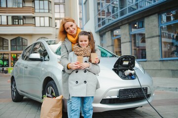 mother with daughter charging electro car at the electric gas station and speak on mobile phone.