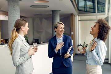 Cheerful female business colleagues having fun while talking in a hallway.