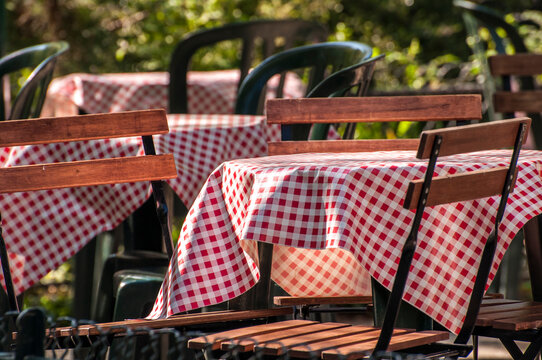 Red and white gingham table cloths cover tables at an outdoor cafe in a garden in Paris France.