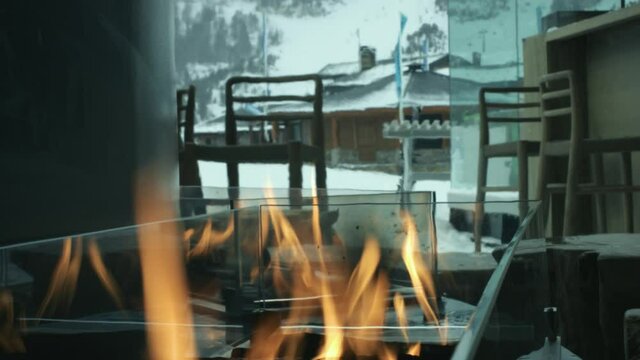 Close view of an indoor fireplace with fire burning. We can see snow in the mountains from the window 4K