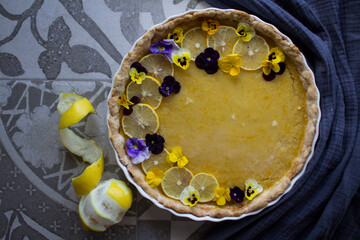 Lemon curd tart decorated with lemon slices and wild pansy flowers. Classic dessert pie top view photo. 
