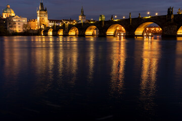 Fototapeta na wymiar illuminated stone monument of Charles Bridge from the 14th century on the Vltava river and lights from street lighting in the center of Prague