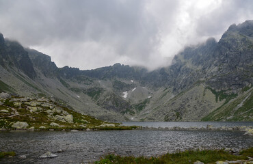 Fototapeta na wymiar The largest mountain lake on slovakian side of High Tatras, Hincovo pleso in Mengusovska valley surrounded by rocky mountains under low clouds