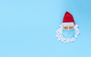 Santa Claus in medical mask on a blue paper. Simple flat lay with copy space.