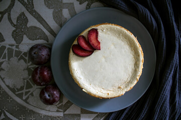 Homemade cheesecake decorated with red plums. Top view photo on grey background with copy space.  
