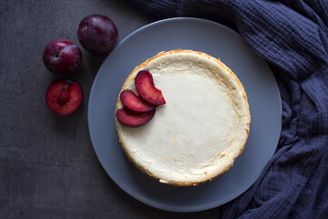 Homemade cheesecake decorated with red plums. Top view photo on grey background with copy space.  
