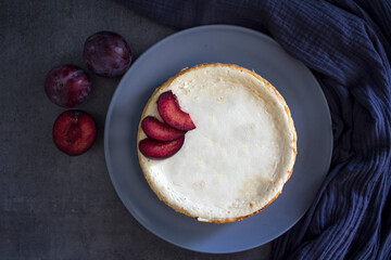 Homemade cheesecake decorated with red plums. Top view photo on grey background with copy space.  
