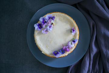Homemade cheesecake decorated with blue wild pansy flowers. Top view photo on grey background with copy space.  
