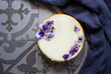 Obraz na płótnie Canvas Homemade cheesecake decorated with blue wild pansy flowers. Top view photo on grey background with copy space. 