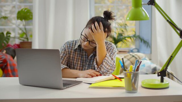 Young exhausted woman trying to study on laptop while little brothers misbehaving on background