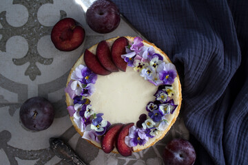 Cheesecake decorated with red plums and wild pansy flowers. Top view photo of classic dessert. 
