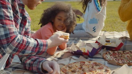 Biracial family enjoying picnic with fast food in park together