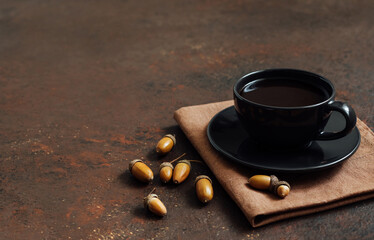 Coffee in a black cup and acorns on a brown background. Acorn coffee without caffeine. Space for text.