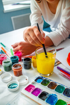 The child lowers his hand into the delta water, washing off the gouache. Home schooling. Drawing training. Children's independence of art. High quality photo