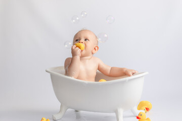 ittle kid likes to swim in a white tub with rubber ducks and foam