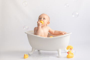 bathing the baby in white bath with foam and rubber ducks