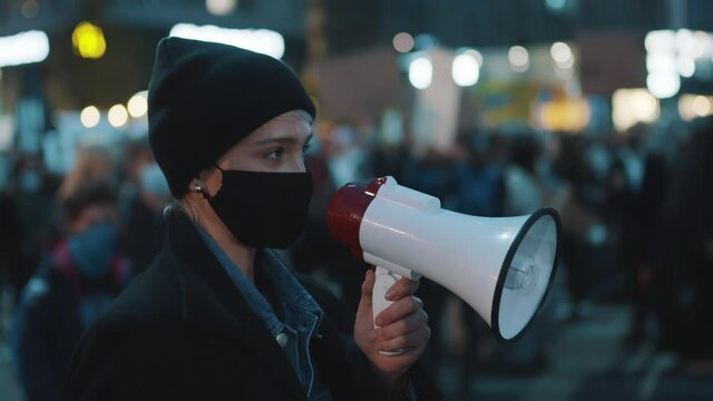  young woman with face mask shouting slogans to loudspeaker at street protest . High quality 4k footage