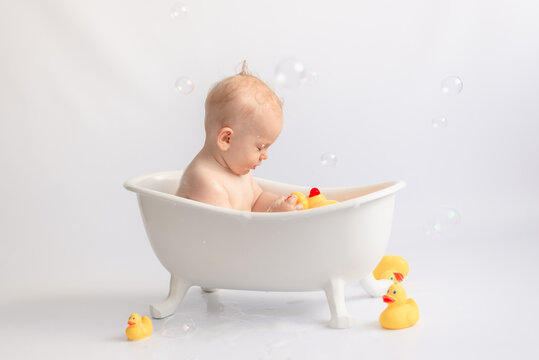 baby bathing toddler in white bath with foam