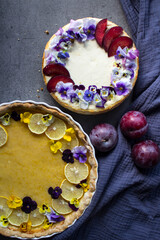 Obraz na płótnie Canvas Lemon tart and cheesecake decorated with edible flowers on yellow fabric background. Sweet food top view photo. 