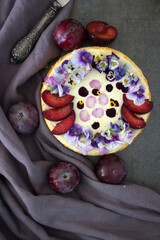 Cheesecake decorated with red plums and wild pansy flowers. Top view photo of classic dessert. 
