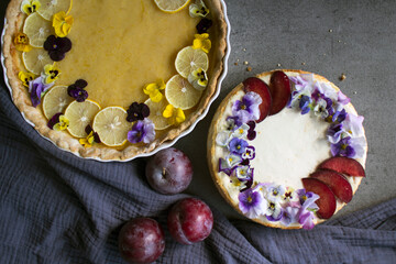 Cheesecake and lemon tart on a table. Two dessert pies decorated with edible flowers. 
