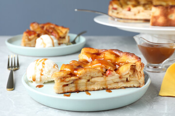 Slice of traditional apple pie with ice cream served on light marble table