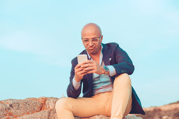 middle aged man with glasses unhappy looking to the cell phone screen sitting outdoors