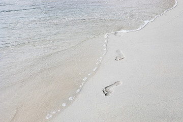 Sea water coming on the white beach sand with footprint