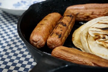 View of some mexican tortillas with fried saussages on a grill