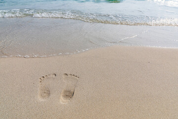 Sea water coming on the white beach sand with footprint