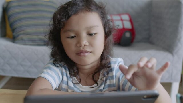 Asian little girl using tablet digital, playing, while sitting in a room 