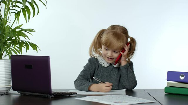 Talk about business. Funny little child girl boss manager emotionally talking on mobile phone, sitting at computer table on white background. Modern kids office. Success, happy childhood. 6k downscale