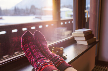 Feet in woollen socks by the Alps mountains view. Woman relaxes by mountain view with a cup of hot...