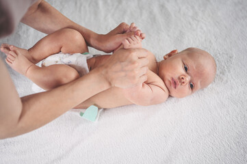 Mother is changing diaper for cute emotional funny newborn little infant baby boy laying in crib