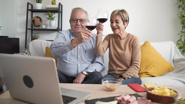 Slow motion of cheerful senior grandparents drinking wine and talking with friends in webcam chat app on laptop screen at home - Elderly family videocall concept