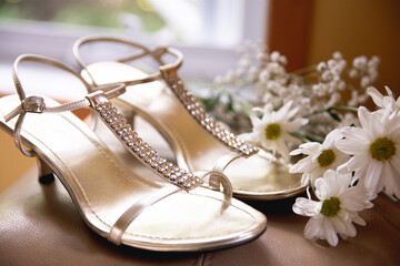 Obraz na płótnie Canvas paire de sandales dorées avec cristaux avec fleurs en arrière plan 