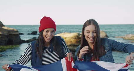 Two happy exchange students standing on beach and holding flag of Great Britain. Two friends laughing by sea. - Powered by Adobe