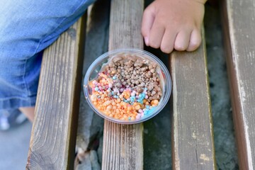 Small ice cream multi-colored ice cream balls in a cup on a bench. Next to the child's hand.