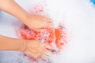 Closeup young Asian woman use hands washing color clothes in basin with detergent have soapy bubble...
