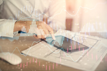 Double exposure of man's hands holding and using a digital device and forex graph drawing. Financial market concept.