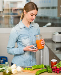 Young woman cooking in home kitchen, preparing vegetable dish with pickled carrot..