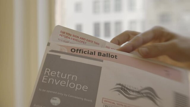 Close-up on woman's hand putting an official election ballot into an envelope for the November 2020 United States local and federal elections. Slow motion with shallow focus, recorded in 4K UHD at 120