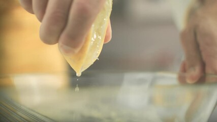 Close up of a lemon being squeezed until lemon juice drops fall into a glass bowl by a vegan chef. Shot in 4K. Shallow depth of field.