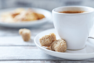 Cup of coffee and brown sugar cubes ( focus on sugar) on bright wooden background. Close up.	