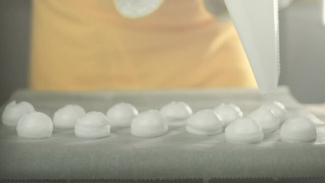 Vegan chef places whipped egg white cream with a icing bag on a backing plate to make meringue. Shot in 4K. Shallow depth of field.