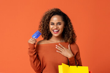 Portrait of smiling young African American woman carrying shopping bag while showing credit card in...